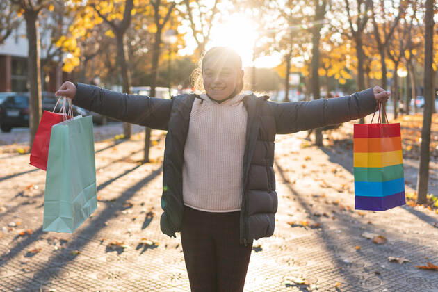 IMAGO Creative: Pride Month 2022, Engagement der Jugendlichen Smiling girl holding shopping bags on footpath model released, JAQF00960