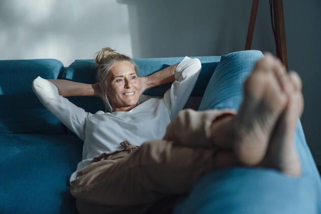 Smiling woman with hands behind head relaxing on sofa model released property released, JOSEF06163