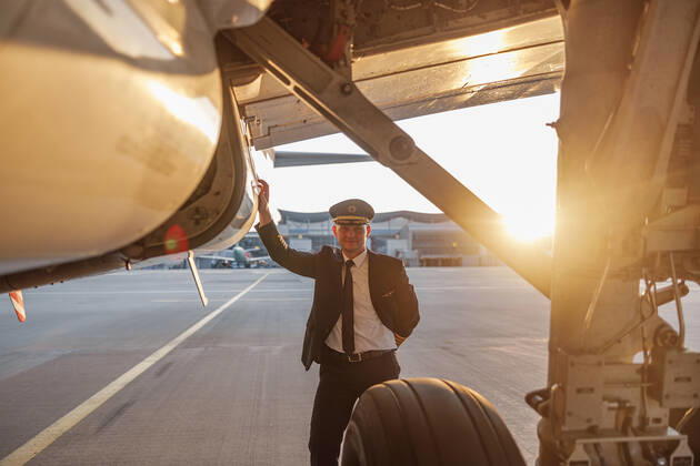Professional male pilot in uniform and hat looking at camera, leaning on a big passenger airplane ready for departure in airport at sunset Professional male pilot in uniform and hat looking at camera, leaning on a big passenger airplane ready for departure in airport at sunset. Aircraft, occupation, transportation concept Copyright: xyaroslavxastakhovx 41017200