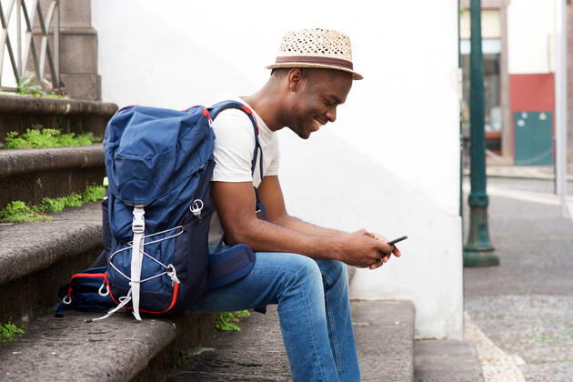 Side portrait of african american male tourist sitting on stairs with bag and mobile phone Copyright: xx 43627150