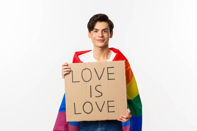 IMAGO Creative: Pride Month 2022, Engagement der Jugendlichen Smiling gay man activist holding sign love is love for lgbt pride parade, wearing Rainbow flag, standing over white background Smiling gay man activist holding sign love is love for lgbt pride parade, wearing Rainbow flag, standing over white background. Copy space Copyright: xSevaxLevitskyx 43848140