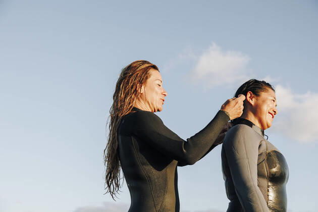 IMAGO Creative: 2022 Sport Favoriten IMAGO Creative: Frühlingsferien und reisen Smiling woman assisting surfer putting on wetsuit at beach model released, MRRF01901