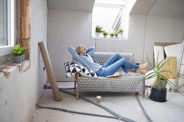 Smiling woman with hands behind head relaxing on sofa in attic model released, Symbolfoto property released, HMEF01347