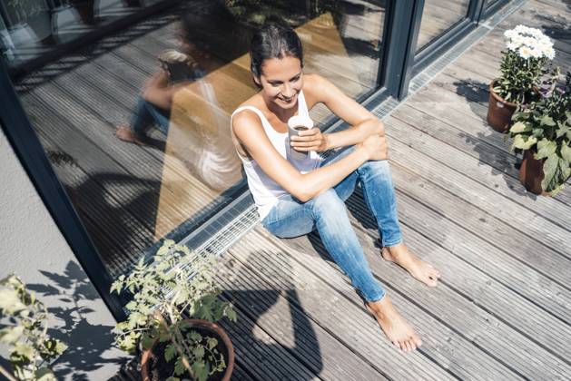 IMAGO Creative, Urban Lifestyle Happy woman with coffee cup sitting in balcony on sunny day model released, Symbolfoto property released, JOSEF07983