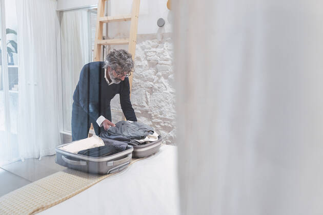 Senior freelancer packing suitcase in bedroom seen through glass model released, Symbolfoto property released, PNAF03598