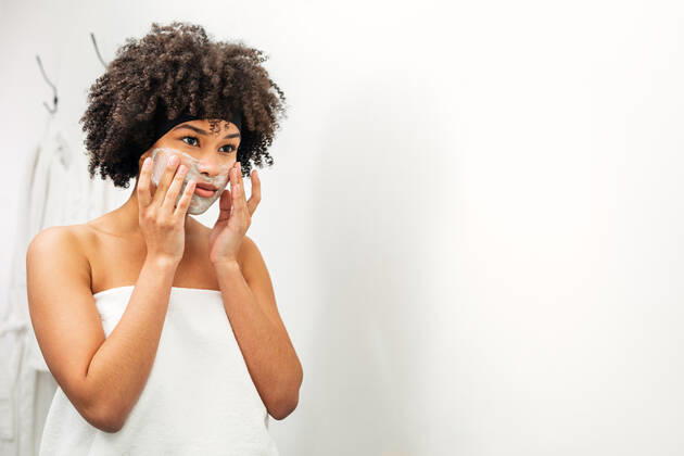 Woman applying facial mask in front of bathroom mirror Copyright: xxArtemxVarnitsinx