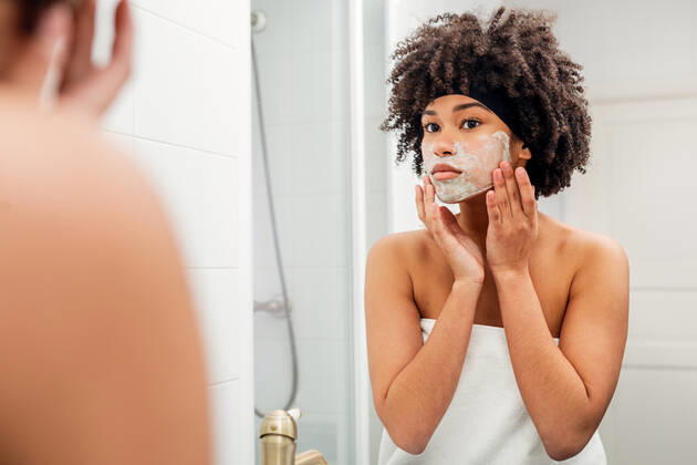 Woman applying facial mask in front of bathroom mirror Copyright: xxArtemxVarnitsinx