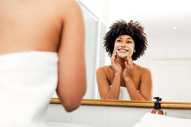 Woman applying facial mask in front of bathroom mirror Copyright: xxArtemxVarnitsinx