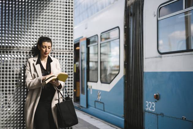 Businesswoman wearing long coat reading book while waiting at railroad station Sweden, Gothenburg, model released Copyright: xMaskotx , MA93969