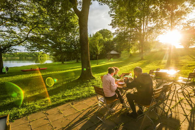 Menschen sitzen in der Abendsonne an einem Tisch einer Gartenwirtschaft und essen, Bayern, Deutschland. Gartenwirtschaft an einem Seeeinem kleinen See