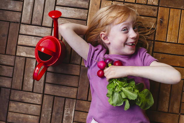 IMAGO Creative, Sommer, Food, Radieschen Happy girl with radish lying by watering can on balcony floor model released, Symbolfoto property released, IHF00839