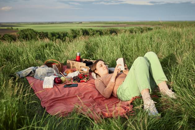 Smiling woman reading book at picnic in field model released, Symbolfoto, ZEDF04592
