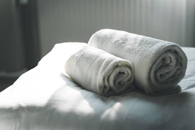 Weiße, gerollte, saubere Handtücher auf dem Hotelbett