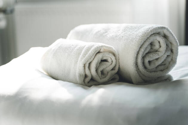 Weiße, gerollte, saubere Handtücher auf dem Hotelbett