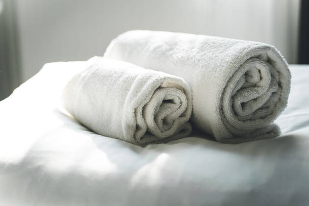 Weiße, gerollte, saubere Handtücher auf dem Hotelbett