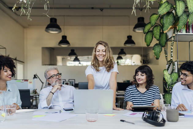 Smiling businesswoman planning strategy on laptop with coworkers in office model released, Symbolfoto property released, MEUF07084