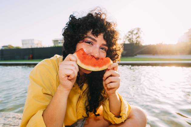 Young woman eating watermelon by pond at sunset model released, Symbolfoto, MEUF07542