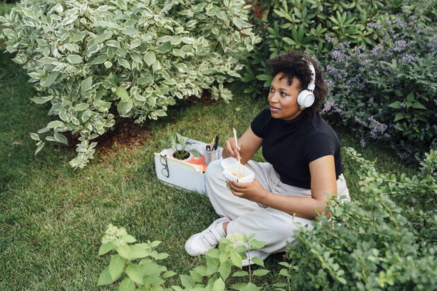 Businesswoman with take out food box listening music through wireless headphones sitting in park model released, Symbolfoto, VPIF06980