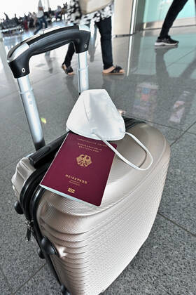 Auf dem Koffer am Flughafen, liegen Reisepass und Mundschutz griffbereit. Im Flugzeug bleibt die Maskenpflicht. München Bayern Deutschland Copyright: xRolfxPossx