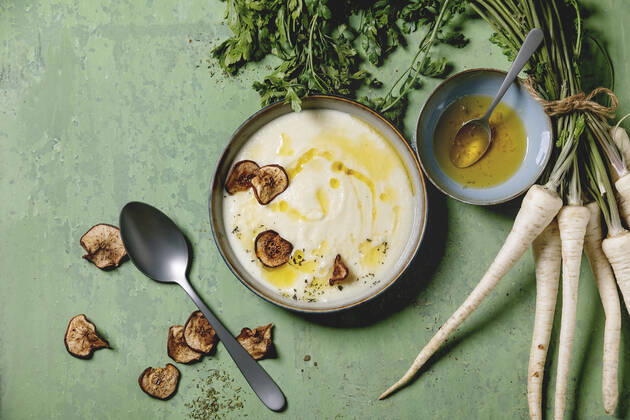 Parsnip soup with butter sauce Parsnip cream soup in ceramic bowl with sun dried pears, butter sauce, bundle of fresh parsnip and herbs over green texture background. Flat lay, space Copyright: xNatashaxBreenx NB300919-7