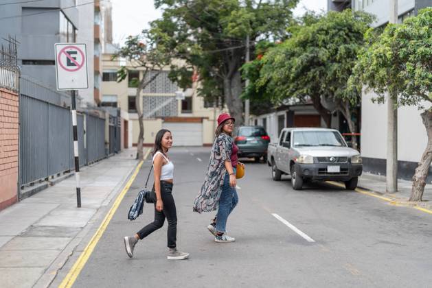 Full body of positive Peruvian female friends crossing the road in a street with parked vehicles and surrounded by trees and buildings, Model released GuillermoSpelucin_SaraiAndPaulaInLima_4 Copyright: xGuillermoxSpelucinx MR