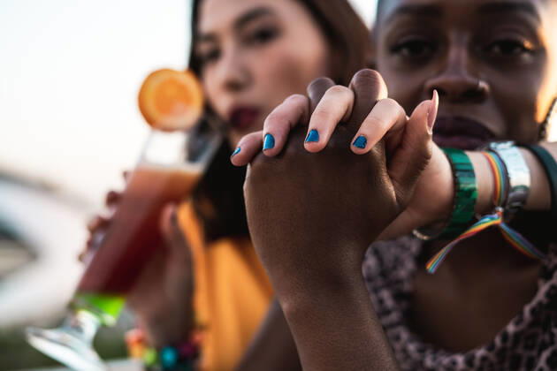 Stylish multiracial girlfriends sitting in open air cafe hugging and holding hands while enjoying refreshing drinks on blurred background, Model released RafaCortes_LesbianEthnicCouple_118 Copyright: xRafaxCortesx MR