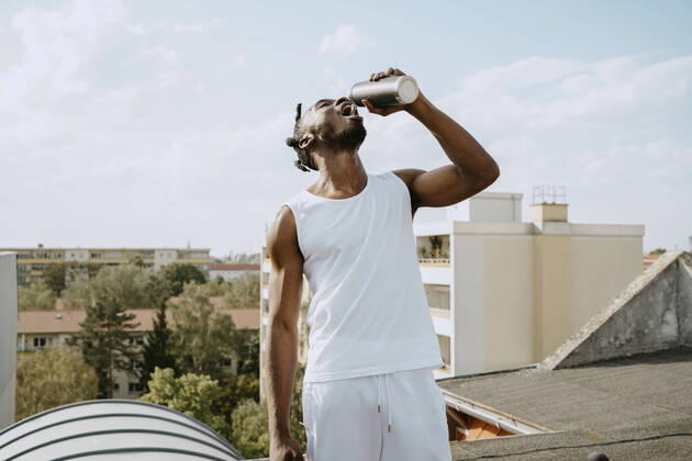 IMAGO Creative: 2022 Sport Favoriten IMAGO Creative: Menschen in Berlin Young man drinking water from bottle while standing on rooftop during sunny day Germany, Berlin, model released, property released Copyright: xMaskot,xMaskotxBildbyraxABx , MA95063 MA95063