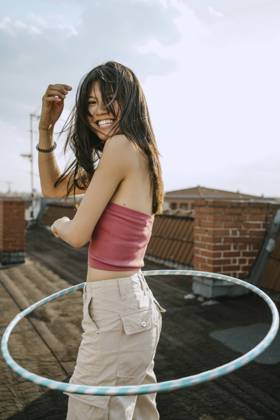 IMAGO Kreativ: Urbane Kultur - Sommer auf den Dächern Side view of cheerful woman spinning hoola hoop on rooftop Germany, Berlin, model released, property released Copyright: xMaskot,xMaskotxBildbyraxABx , MA95088 MA95088