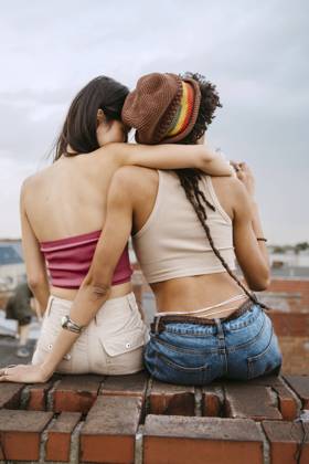 IMAGO Kreativ: Urbane Kultur - Sommer auf den Dächern Rear view of young woman embracing female friend wearing knit hat while sitting on rooftop Germany, Berlin, model released, property released Copyright: xMaskot,xMaskotxBildbyraxABx , MA95129 MA95129