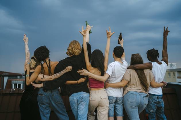 IMAGO Kreativ: Urbane Kultur - Sommer auf den Dächern Rear view of multiracial young men and women gesturing with arms raised on rooftop at dusk Germany, Berlin, model released, property released Copyright: xMaskot,xMaskotxBildbyraxABx , MA95156 MA95156