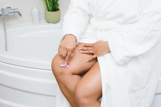 Crop unrecognizable female in bathrobe shaving legs with razor while doing skin care routine in bathroom, Model released AngelaRober_AnnyPersonalCare_30 Copyright: xAngelaxRoberx MR