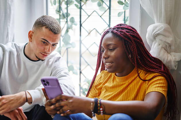 Multiracial couple looking at the mobile sitting on the floor at home Valencia, Valencian Community, Spain CR_VFKDPR221019-1058204-01 ,model released, Symbolfoto