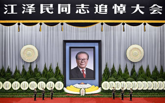 (221206) -- BEIJING, Dec. 6, 2022 -- A memorial meeting for Jiang Zemin, who passed away on Nov. 30 at the age of 96, is held in the Great Hall of the People in Beijing, capital of China, Dec. 6, 2022. The meeting was held by the Communist Party of China (CPC) Central Committee, the Standing Committee of the National People s Congress, the State Council, the National Committee of the Chinese People s Political Consultative Conference, and the Central Military Commission. Jiang s casket, covered with the flag of the CPC, was placed amidst bouquets of flowers and sprigs of evergreen cypress. A floral arrangement presented by family members of Jiang, including his wife Wang Yeping, was placed in front of the casket, flanked by six guards