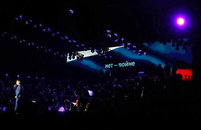 Night of the Proms 2022 13.12.2022, Erfurt, Messehalle, Night of the Proms 2022 Das Antwerp Philharmonic Orchestra und der Chor Fine Fleur unter Leitung der Dirigentin Alexandra Arrieche begleiten die Stars im Bild: Moderator Marcus Fahn auf der Buehne, im Hintergrund ist fuer einen Moment die russische Flagge eingeblendet, darauf steht in kyrillischen Buchstaben Nie wieder Krieg