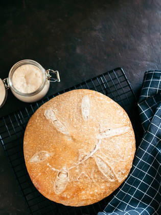 Wheat round sourdough bread, copy space, top view Wheat round sourdough bread and sourdoug starter in glass jar. Top view of delicious homemade sourdough bread on black background with copy space. Home made sourdough bread making concept. Vertical. Copyright: xZoonar.com OlgaxSergeevax 17540774