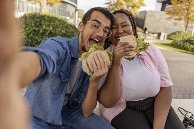Happy young couple eating sandwich and taking selfie at footpath model released, Symbolfoto, JCCMF08076