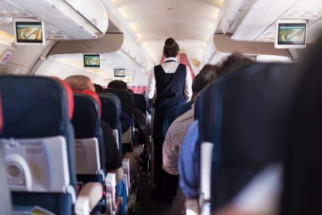 Interior of commercial airplane with passengers on seats during flight. Interior of commercial airplane with passengers on seats during flight. Stewardess in dark blue uniform walking the aisle. Horizontal composition. Copyright: xZoonar.com MatejxKastelicx 11011825