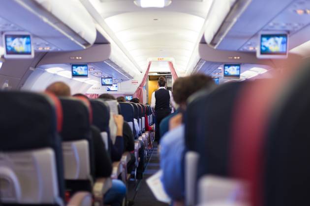 Interior of commercial airplane with passengers on seats during flight. Interior of commercial airplane with passengers on seats during flight. Stewardess in dark blue uniform walking the aisle. Horizontal composition. Copyright: xZoonar.com MatejxKastelicx 11027422