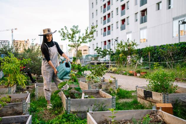IMAGO Creative, Urban Lifestyle Smiling young woman wearing hat watering plants in urban garden model released, Symbolfoto, GDBF00022