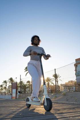 From below pensive young African American female in casual clothes and protective helmet looking away while riding electric scooter on city street with palm trees, Model released OscarDeDios_ID12835_390045_005 Copyright: xOscarxdexDiosx MR