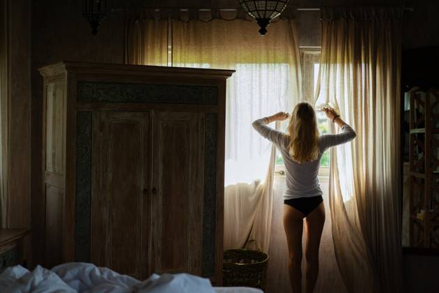 A young woman opens the curtains in the morning. South Kuta, Bali, Indonesia CR_YUKI230707-1213022-01 ,model released, Symbolfoto