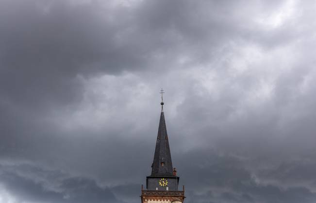 Dunkle Wolken über dem Kirchturm Dunkle Wolken eines Gewitters sind am Nachmittag am Himmel über dem Turm der katholischen Kirche St. Ursula zu sehen., Oberursel Hessen Deutschland