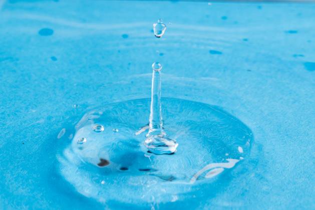 Close up of water drop falling into water with ripples and copy space on blue background. Water, liquid and colour concept. Copyright: xx 4132833