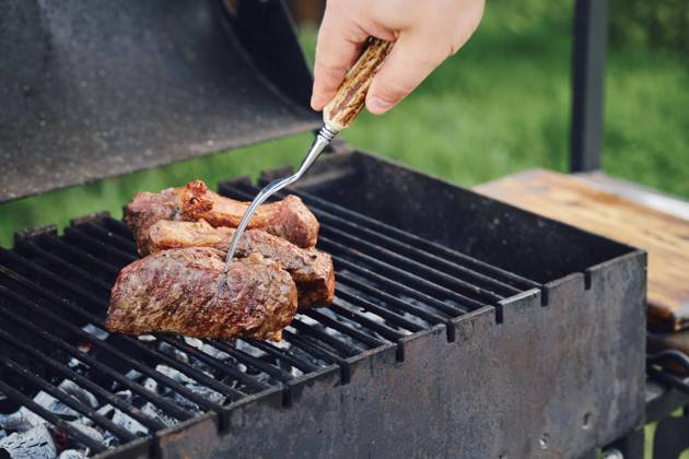 Unbekannter Mann beim Grillen eines Steaks im Freien. Er wendet das Fleisch mit einer Gabel