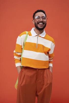 Young man with hands in pockets standing against orange background model released, Symbolfoto, EKHF00065
