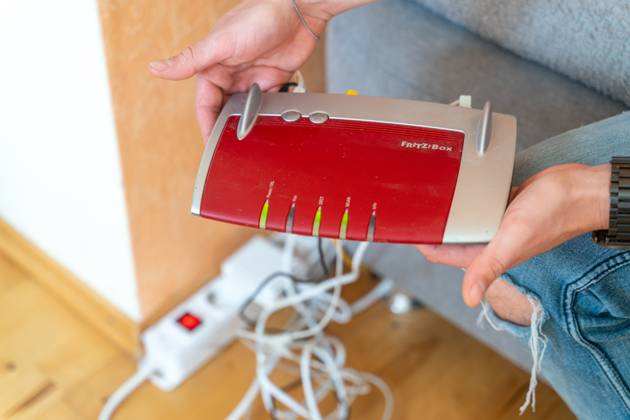 Ein Fritzbox Wlan Router in einer Wohnung. Mann hält den Fritz Box Router in der Hand