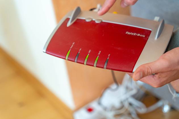 Ein Fritzbox Wlan Router in einer Wohnung. Mann hält den Fritz Box Router in der Hand