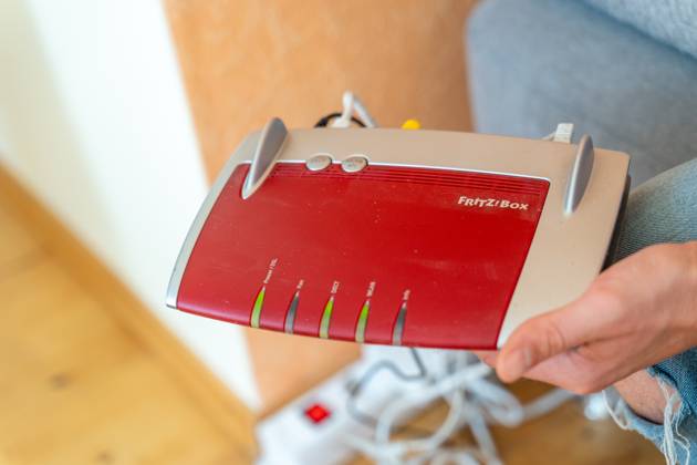 Ein Fritzbox Wlan Router in einer Wohnung. Mann hält den Fritz Box Router in der Hand