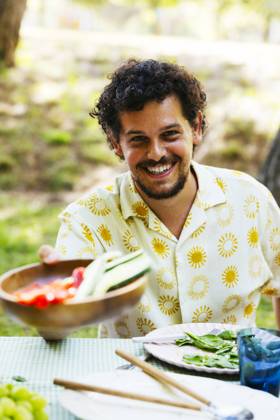 Smiling man offering food at picnic table in garden model released, Symbolfoto, EBSF03751