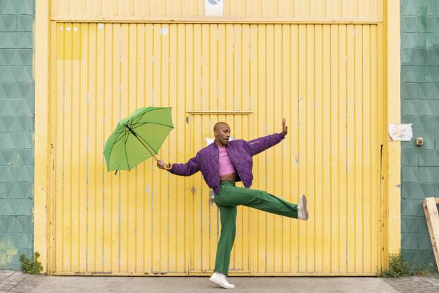 Non-binary person dancing with green umbrella in front of yellow shutter door model released, Symbolfoto, AFVF09352